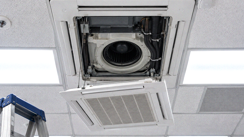 Ceiling cassette indoor unit with its panel lowered, seen from below in an open office